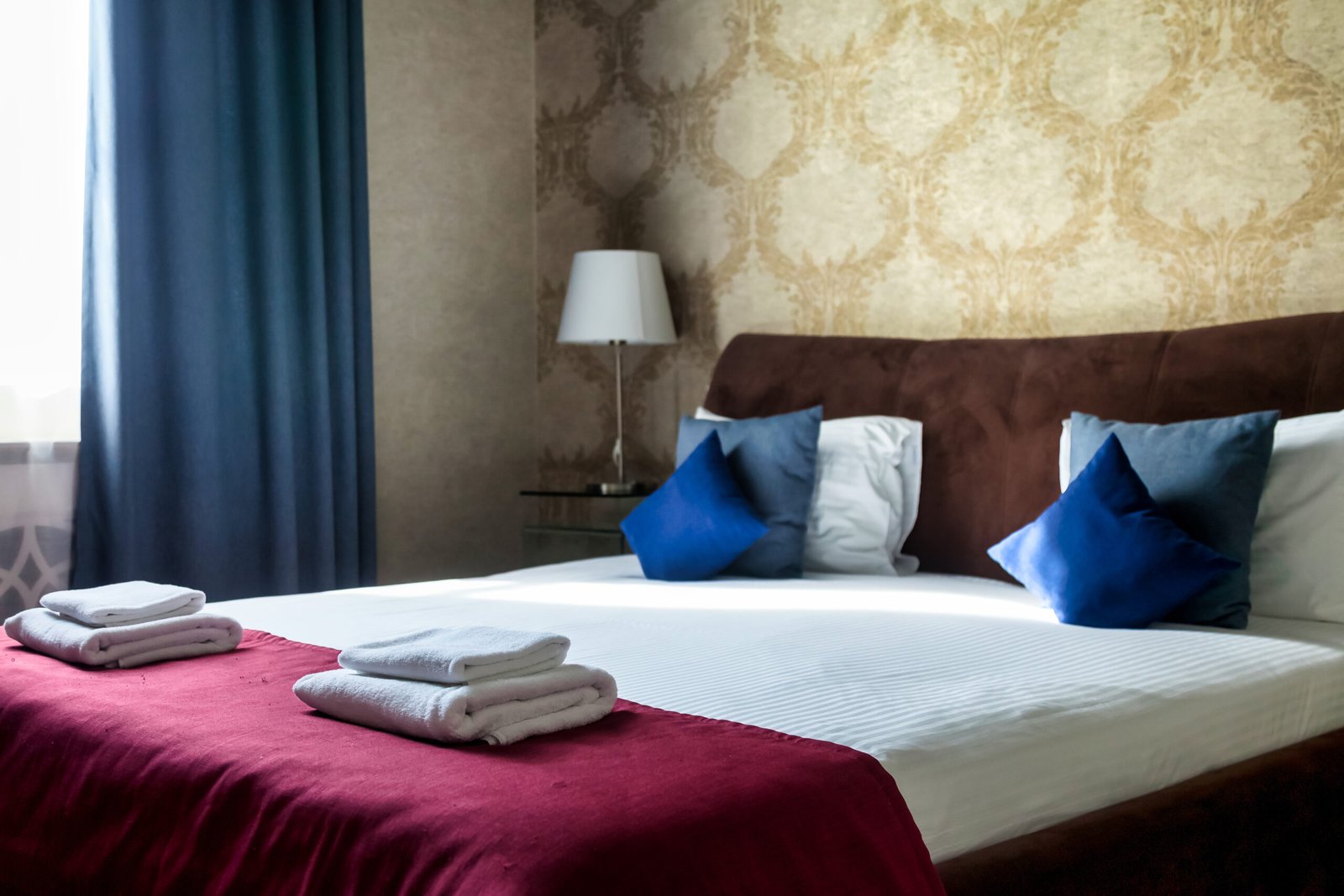 A well-appointed bedroom features a large bed with crisp white linens and colorful pillows. Soft lighting and decorative wallpaper create a serene indoor atmosphere ideal for comfort.