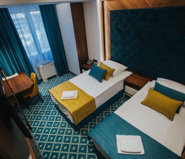 Hotel room with a two single bed with yellow and blue cushions and folded towels