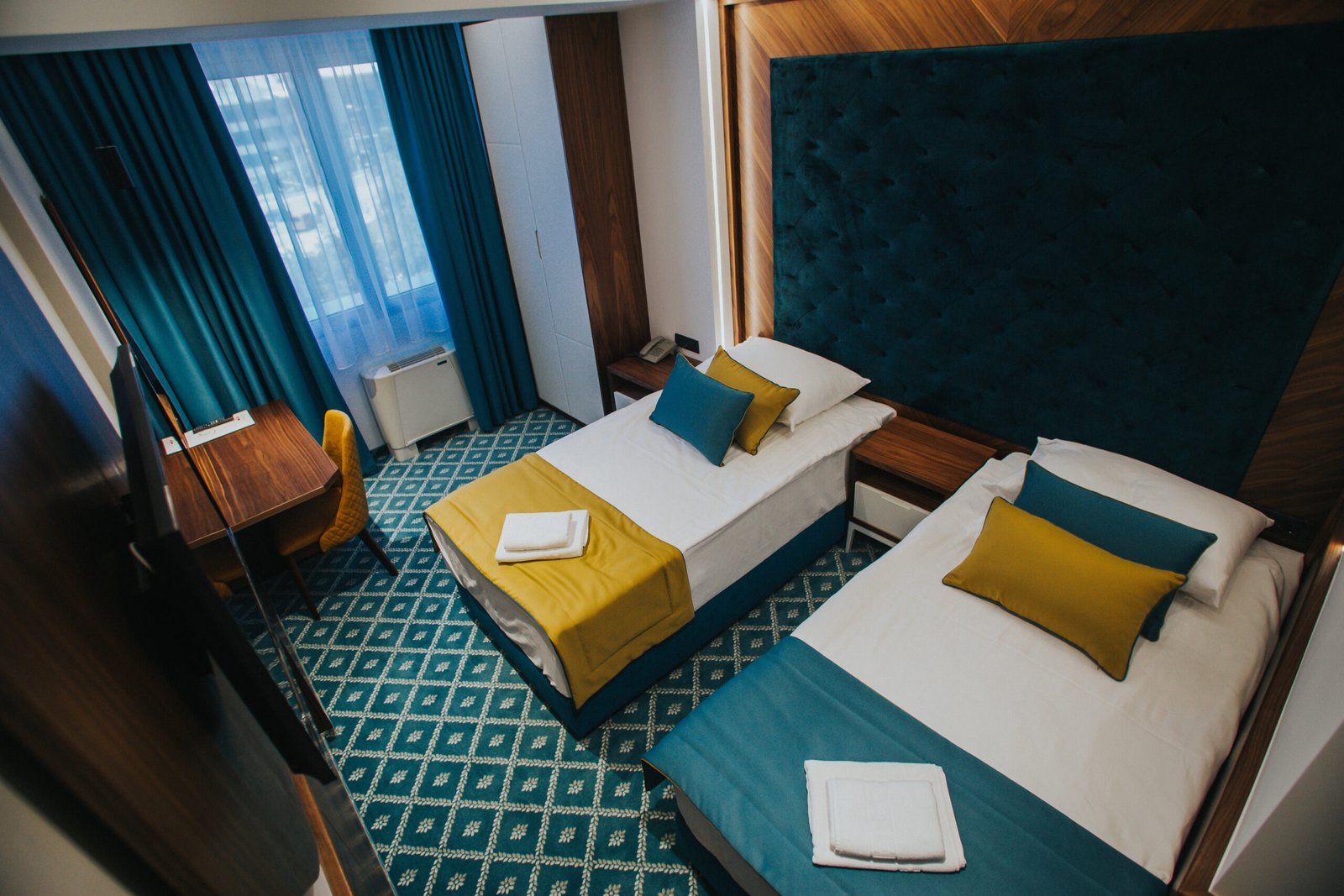 A hotel room with a two single beds with yellow and blue cushions and folded towels
