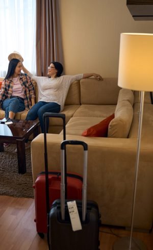 Two smiling female tourists sitting on comfortable sofa by window in suite