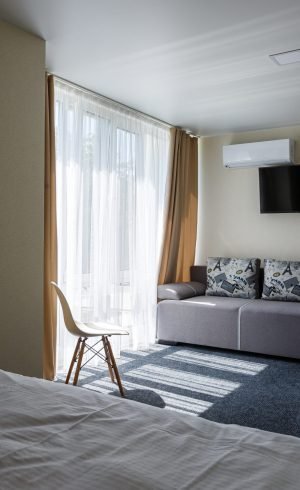 Large gray sofa in the hotel room with a TV and large windows